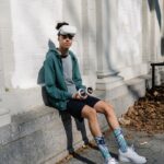Full body of young male in sportswear and VR goggles sitting on concrete foundation of white building and holding controllers